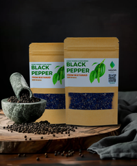 Two Naturish Elite hand‑picked sun‑dried black pepper 100 g kraft pouches from Wayanad, with a stone mortar spilling peppercorns on a wooden board.