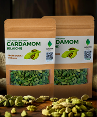 Two Naturish hand‑picked sun‑dried cardamom (elaichi) 100 g kraft pouches filled with green cardamom pods, surrounded by loose pods on a wooden surface.