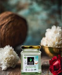 Naturish Elite cold pressed virgin coconut oil 250 ml glass jar with golden lid placed on a wooden table surrounded by white and red flowers in a luxe setting.
