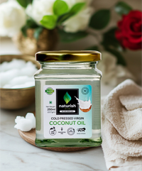 Naturish Elite cold pressed virgin coconut oil 250 ml glass jar with golden lid placed on a wooden coaster, surrounded by soft towels, coconut pieces and flowers.