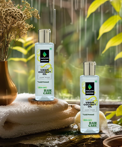 Two Naturish Elite cold pressed virgin coconut oil bottles for skin and hair care placed on fluffy white towels by a rainy window in a spa-like setting.