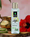  Naturish Elite cold pressed virgin coconut oil bottle for skin and hair care placed on a wooden slab with aloe vera slices and a red hibiscus flower.