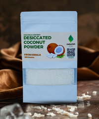 Single Naturish desiccated coconut powder 100g pouch standing on table with coconut flakes scattered in front