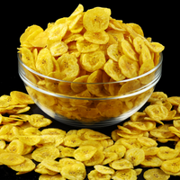 Glass bowl overflowing with crispy golden banana chips, with more chips scattered around on a black background.