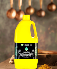 Bright yellow 1‑litre Naturish coconut oil can with black label, rustic wooden table and blurred copper ladles in warm kitchen background.
