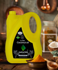Bright yellow 5‑litre Naturish coconut oil can with black label on rustic table, coconuts and spices softly blurred in background.