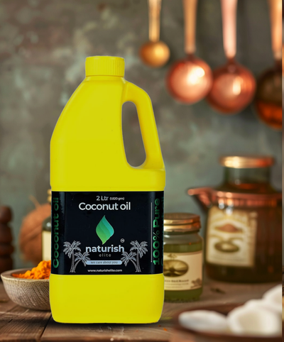 Bright yellow 2‑litre Naturish coconut oil can with black label on a rustic kitchen table, jars and utensils softly blurred behind.