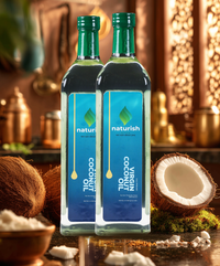 Two Naturish Elite virgin coconut oil bottles with blue labels and coconuts on a warm rustic kitchen counter.